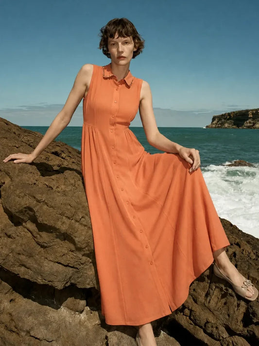 Woman in an orange dress standing on a rocky beach with ocean and sky in the background