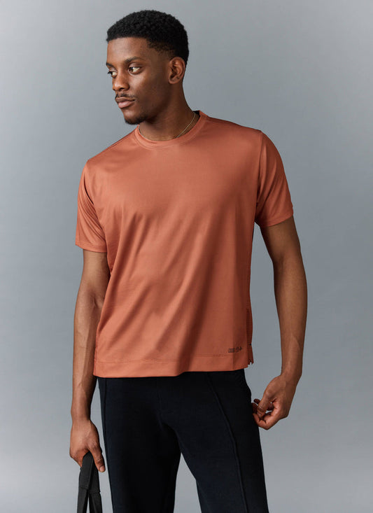 A model wears the Percival PCVL Performance Top in rust, styled with black trousers against a studio background.