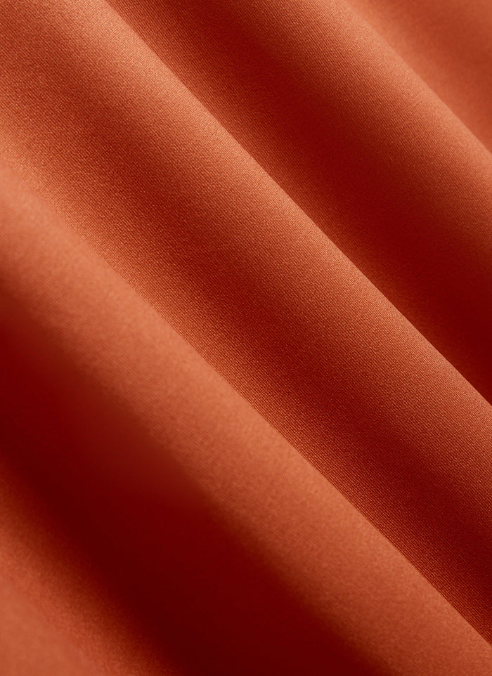 A close-up of the textured, rust-coloured, moisture-wicking fabric of the Percival PCVL Performance Top.