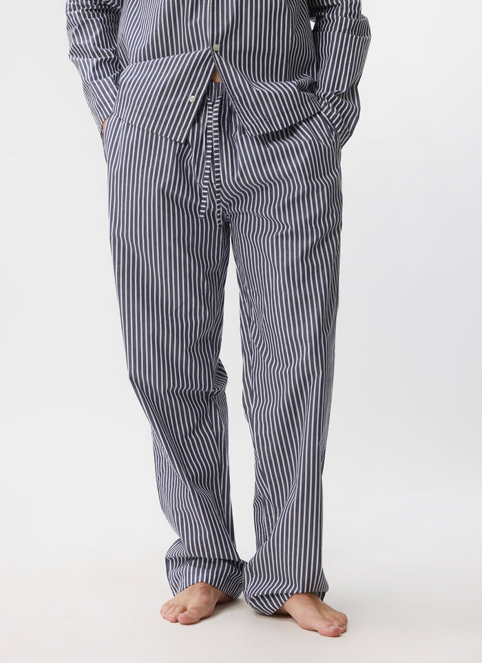 A man models the blue and white striped cotton pyjama bottoms from Percival against a white studio background.