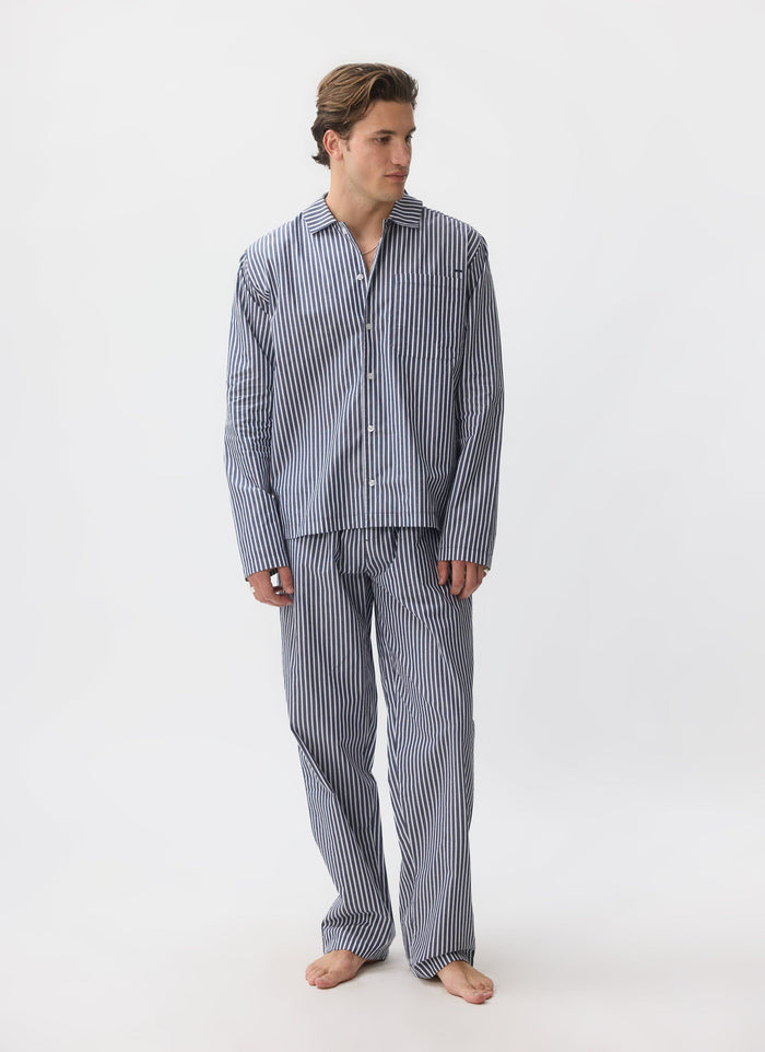 A full-length studio shot of a model wearing the blue and white striped cotton pyjama set from Percival.