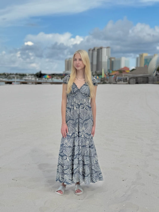 Woman in a long dress standing on a sandy beach with buildings in the background