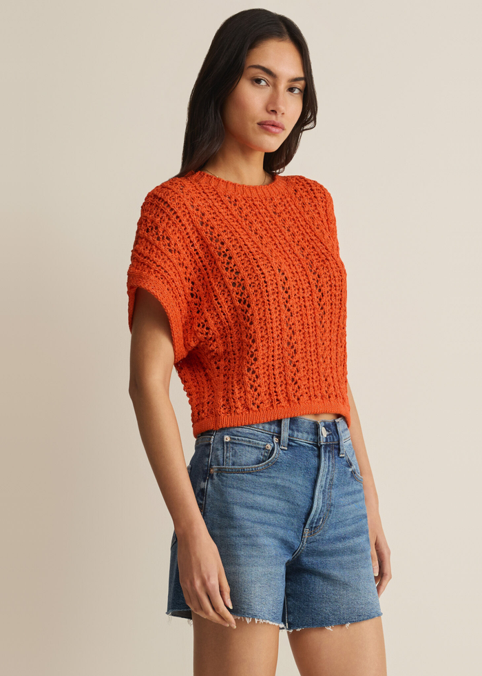 Woman wearing an orange crochet top with denim shorts