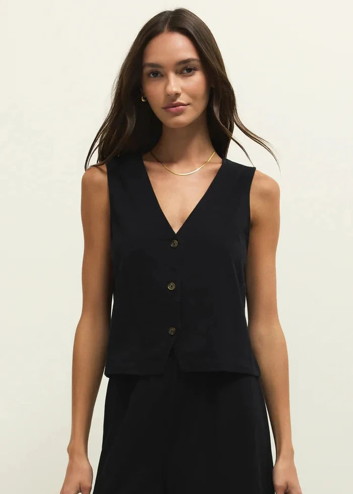Woman wearing a black sleeveless top with buttons on a plain background